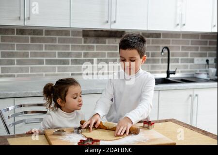 Die Kinder machen Weihnachtskekse. Der Junge rollt den Teig mit einem Nudelholz aus. Stockfoto