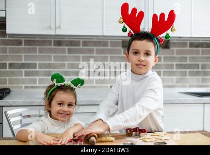 Die Kinder mit Weihnachtsschmuck auf dem Kopf bereiten aus dem Teig WeihnachtsLebkuchen zu. Vorbereitung auf Weihnachten. Stockfoto