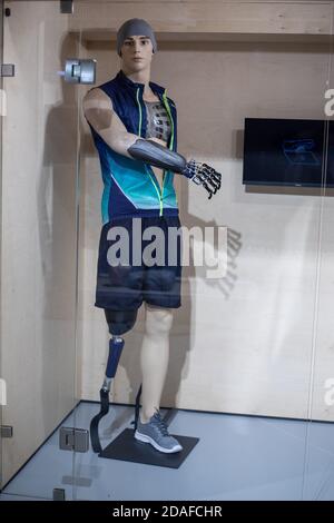 Eine Schaufensterpuppe in Form eines jungen Mannes in Sportbekleidung mit einem prothetischen Arm und Bein hinter Glas. Demonstration neuer Technologien in der Prothetik Stockfoto