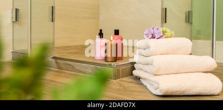 Begehbare Dusche ohne Duschwanne. Im Vordergrund sind Frottee-Handtücher und duftende Lotionen. Wellness-Atmosphäre im Bad. Stockfoto