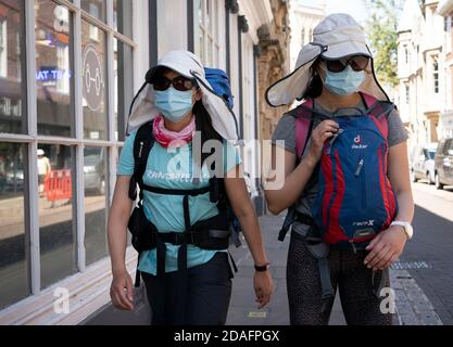 Zwei Touristen, die in Legionairres Hüten und Gesichtsmasken gekleidet sind, gehen während der COVID 19 Pandemie 2020 durch das Stadtzentrum von Cambridge Stockfoto