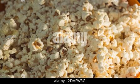 Frisches heißes Popcorn liegt in einer orangefarbenen Schüssel. Kino Pop Mais Hintergrund. Stockfoto