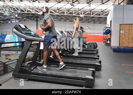 Fit afroamerikanischen Mann trägt Gesichtsmaske und Kopfhörer laufen Auf dem Laufband tun Cardio-Training Stockfoto