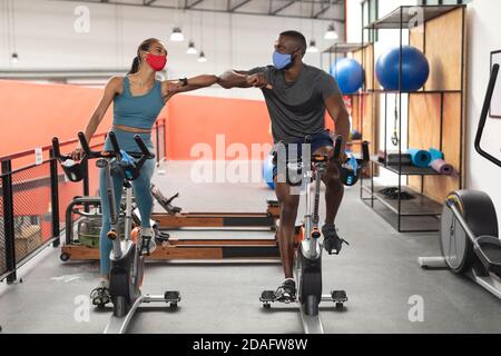 Fit afroamerikanischen Mann und fit kaukasischen Frau trägt Gesicht Masken, die sich gegenseitig durch Berühren begrüßen Stockfoto