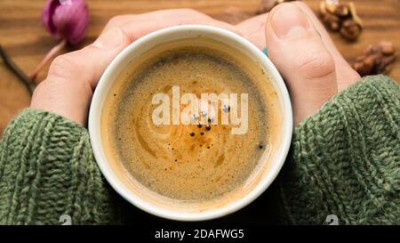 Die Hände eines Mannes halten eine Tasse aromatischen Kaffee in der Hand. Eine Tasse aromatischen Kaffee steht auf einem Holztisch. Ein aromatischer Kaffee mit Schaum. Belebend Stockfoto