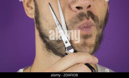 Schöner junger Kerl trimmt seinen Bart mit einer Schere. Stockfoto