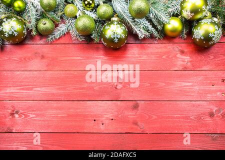 Weihnachtskarte, Tapete auf rotem alten Holzhintergrund. Verschneite Nadeln und grüne weihnachtskugeln als Dekoration. Leerzeichen für Text. Stockfoto