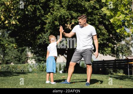 Vorschulkinder Junge und junge Erwachsene Mann in Sportkleidung geben jeder Andere hohe fünf im Park Stockfoto