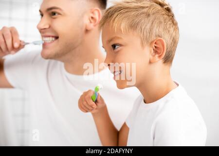 Lächelnder Junge mit Zahnbürste, die Zähne zeigt, während er wegschaut Verschwommener Mann auf dem Hintergrund Stockfoto