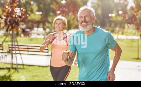 Wir kommen voran. Aktives reifes Familienpaar in Sportswear, das konzentriert beim Laufen im Park an einem warmen sonnigen Tag aussieht. Fröhliches Seniorenpaar Stockfoto