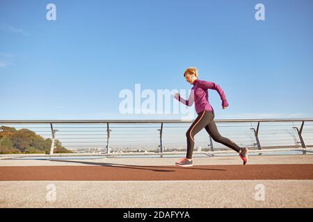 Gesundheit steht an erster Stelle. In voller Länge Schuss von motivierten aktiven reifen Frau in Sportswear Laufen im Freien an einem sonnigen Tag. Seitenansicht Stockfoto