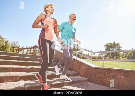 Stärken Sie Ihren Morgen. Ganzkörperaufnahme eines aktiven, reifen Familienpaares in Sportswear, das an einem sonnigen Morgen gemeinsam im Park läuft. Freudiger Senior Stockfoto