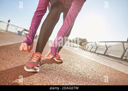 Vorbereitung. Kurze Aufnahme einer aktiven reifen Frau, die Sportkleidung trägt und ihre Schnürsenkel bindet, während sie sich für das Laufen im Freien an einem sonnigen Tag vorbereitet Stockfoto