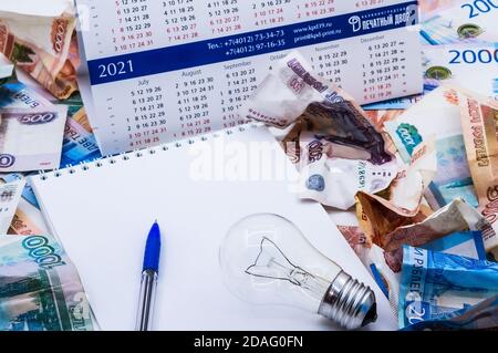 Glühbirne und Kalender, Lampe und Geld, zerknittertes Geld und Notepad, zerknittertes russisches Geld Stockfoto
