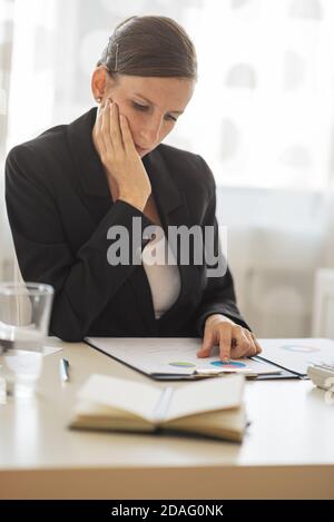 Junge Geschäftsfrau, die an ihrem Schreibtisch sitzt und Dokumente und Berichte in einem Clip-Ordner betrachtet. Stockfoto