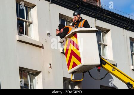 Zwei Männer, die in der Höhe in einem Kirschpflücker arbeiten und an einer weißen Hausfront arbeiten. Stockfoto