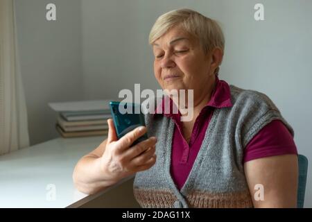 Eine alte Frau benutzt ein Handy. Eine ältere Frau ruft auf einem Smartphone an, während sie zu Hause in einem Raum sitzt. Stockfoto
