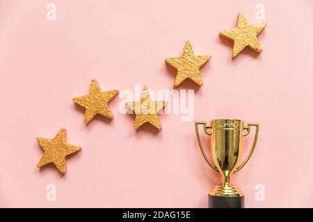 Einfach flacher Lay-Design-Gewinner oder Champion Gold Trophäe Cup und 5-Sterne-Bewertung isoliert auf pinkfarbenem Pastellhintergrund. Sieg erster Wettkampfplatz. Erfolgskonzept. Kopierbereich in der Draufsicht Stockfoto