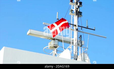 Dänische Flagge auf modernem Schiff neben Navigation und Antenne und Radarausrüstung gegen blauen Himmel. Stockfoto