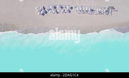 Luftaufnahme von oben auf leeren Sandstrand und türkisfarbenes Meer, mit Sonnenschirmen und Liegestühlen auf weißem Sand in schönen sonnigen Sommertag. Stockfoto