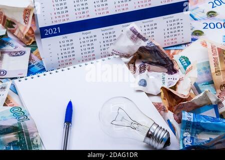 Glühbirne und Kalender, Lampe und Geld, zerknittertes Geld und Notepad, zerknittertes russisches Geld Stockfoto