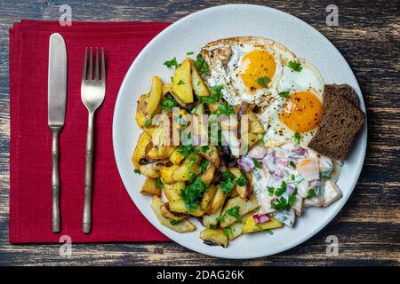 Traditionelles ukrainisches Essen, Bratkartoffeln mit Zwiebeln, Spiegeleier, Gemüsesalat, Schwarzbrot auf Holzhintergrund, Nahaufnahme, Draufsicht Stockfoto