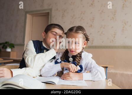 Zwei Studenten, ein Junge und ein Mädchen sitzen bei einem Schreibtisch in der Schule und kommunizieren miteinander in der Ohr Stockfoto