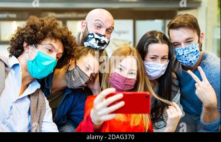 Lächelnde Gruppe von Menschen tragen schützende Gesichtsmaske posiert für Ein Bild zusammen vor einem Smartphone.Glückliche Social Influencer Ein Selfie machen Stockfoto