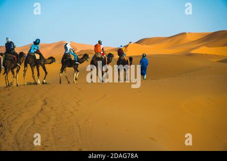 Merzouga, Marokko - APRIL 29 2019: Touristen auf einem Kamelritt Tour in der Sahara Wüste Stockfoto