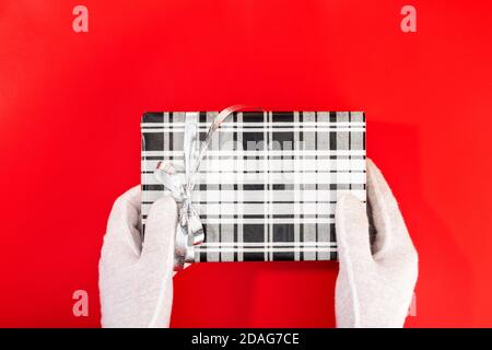 Weihnachtsmann mit Handschuhen hält ein Weihnachtsgeschenk auf rotem Hintergrund. Speicherplatz kopieren. Stockfoto