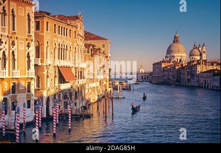 Canal Grande in Venedig und Gondeln mit der Kuppel der Basilica di Santa Maria della Salute. Zeitlos klassischer, ikonischer Blick auf die Landschaft mit Gondoliern, die im späten Nachmittagssonne Venedig Italien entlang des Canale Grande fahren Stockfoto