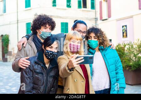 Glückliche Gruppe von Freunden tragen schützende Gesichtsmaske unter einem Selfie in der Stadtstraße nach der Wiedereröffnung der Sperre.Multiethnische Männer Und eine Frau Stockfoto