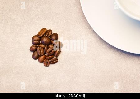 Ein kleiner Haufen gerösteter Kaffeebohnen, der nahe an liegt Die Seite einer leeren Kaffeetasse Stockfoto