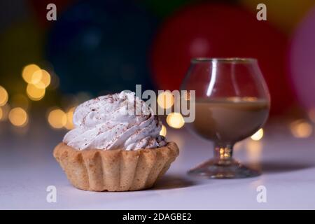 Festlicher Cupcake und ein Glas mit einem braunen Flüssiglikör. Auf dem Hintergrund von bunten Ballons und Lichter. Party, Geburtstagskonzept. Speicherplatz kopieren. Hochwertige Fotos Stockfoto