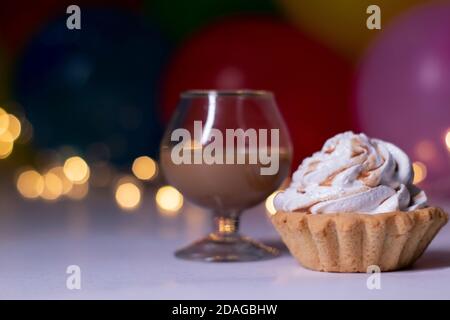 Festlicher Cupcake und ein Glas mit einem braunen Flüssiglikör. Auf dem Hintergrund von bunten Ballons und Lichter. Party, Geburtstagskonzept. Speicherplatz kopieren. Hochwertige Fotos Stockfoto