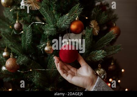 Frau hält rote Ornament aus der Nähe, Winter Urlaub Vorbereitungen. Dekorieren weihnachtsbaum mit modernen roten Kugel in festlich dekorierten Raum. Frohe Ch Stockfoto