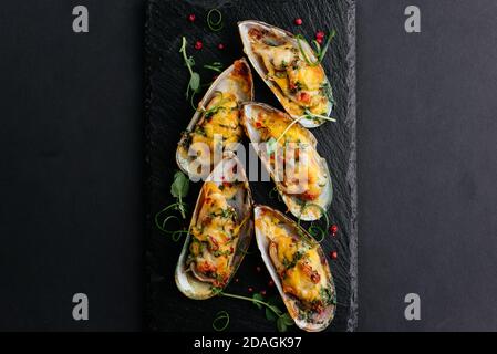 Gebackene Muscheln mit Käse und Gemüse auf schwarzem Hintergrund Stockfoto