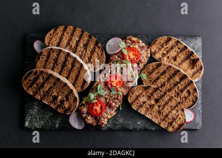 Rindertartare mit Roggencroutons auf schwarzem Hintergrund Stockfoto