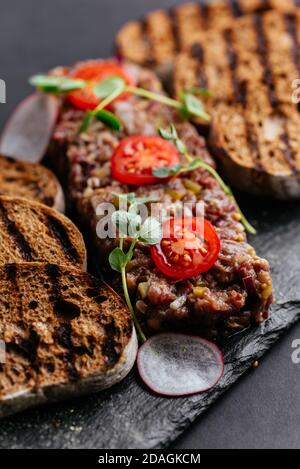 Rindertartare mit Roggencroutons auf schwarzem Hintergrund Stockfoto