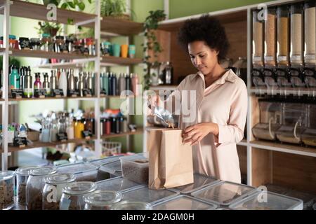 Schwarze Frau Füllung Papierbeutel mit Bio-Pasta während der Arbeit Im Ökoladen Stockfoto