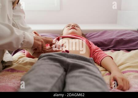 Ärztin untersucht den Bauch eines kleinen Mädchens in ihrem Zimmer. Hausarzt Konzept Stockfoto