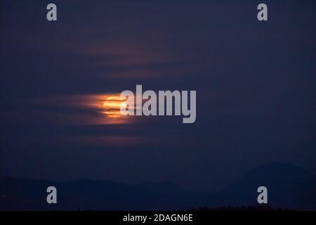 Riesiger oranger Vollmond, der durch neblige Wolken den Nachthimmel um ihn herum erhellt und eine mystische, unheimliche Atmosphäre schafft. Super Mond. Stockfoto