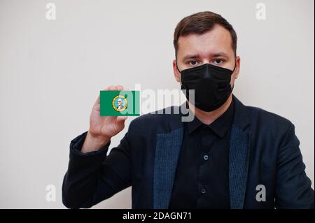 Mann tragen schwarz formell und schützen Gesichtsmaske, halten Washington Flagge Karte isoliert auf weißem Hintergrund. USA Coronavirus Covid Länderkonzept. Stockfoto