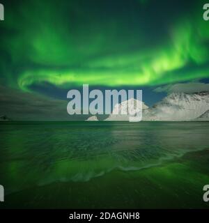 Nordlichter - aurora borealis leuchten am Himmel über Vik Strand und verschneiten Bergen, Vestvågøy, Lofoten Inseln, Norwegen Stockfoto