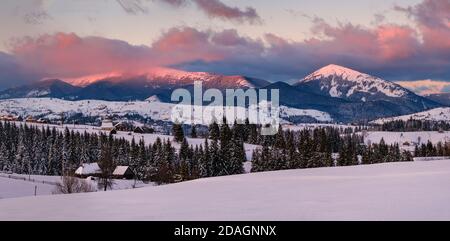 Alpendorf Außenansicht am letzten Abend Sonnenuntergang Sonne Licht. Winter verschneite Hügel und Tannen, herrliche und malerische Bergkette in f Stockfoto