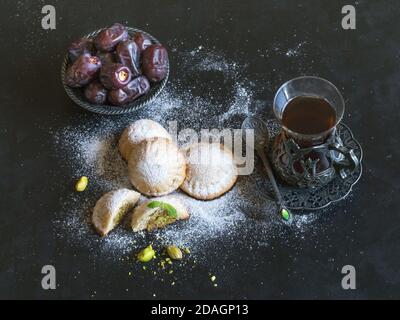 Ägyptische Kekse 'Kahk El Eid' mit Datteln und einer Tasse Tee auf einem schwarzen Tisch serviert. Cookies von El Fitr Islamischen Fest. Stockfoto