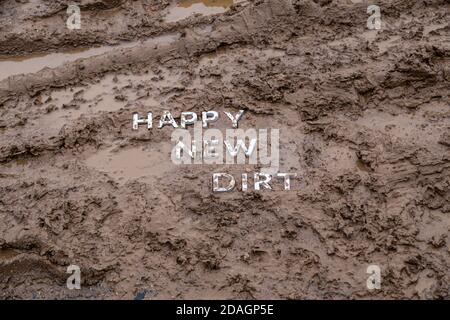 Die Worte glücklich neuen Schmutz gelegt mit silbernen Metall-Buchstaben Auf nasser Schlammoberfläche in diagonaler Perspektive unter bewölktem Herbst Tageslicht Stockfoto