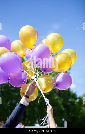 Vertikale Aufnahme von frisch vermählten Paaren mit gelbem und violettem Helium Luftballons am Himmel Stockfoto