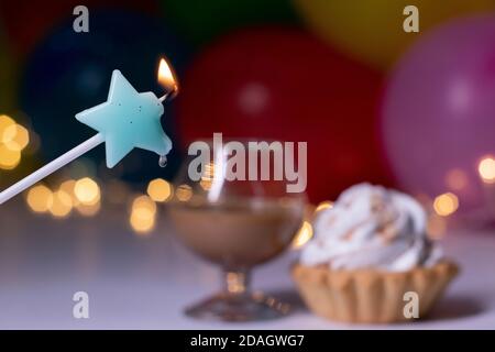 cupcake mit einer blauen Sternkerze und einem Glas mit einem braunen Flüssiglikör. Auf dem Hintergrund von bunten Ballons und Lichter. Party, Geburtstagskonzept. Speicherplatz kopieren. . Hochwertige Fotos Stockfoto