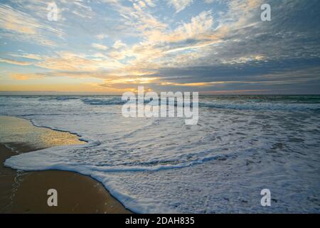 Goldener Sonnenuntergang am Strand und niedrige Meereswellen bremsen das Ufer. Ruhige Szene, schöner wolkig Himmel auf dem Hintergrund Stockfoto